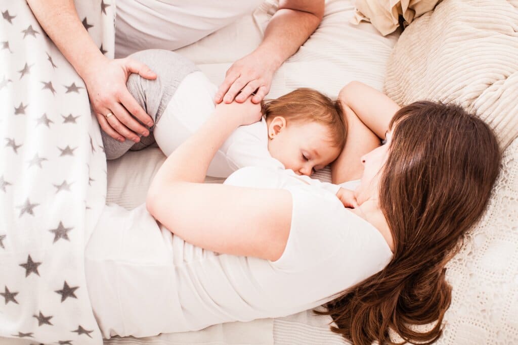 Parents in bed with breastfeeding child between them.