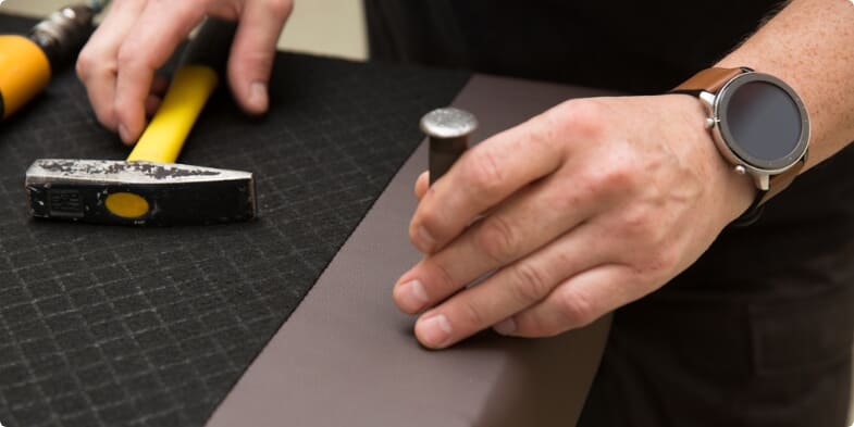 Close up of man's hands holding a hammer and pin, assembling a divan bed.