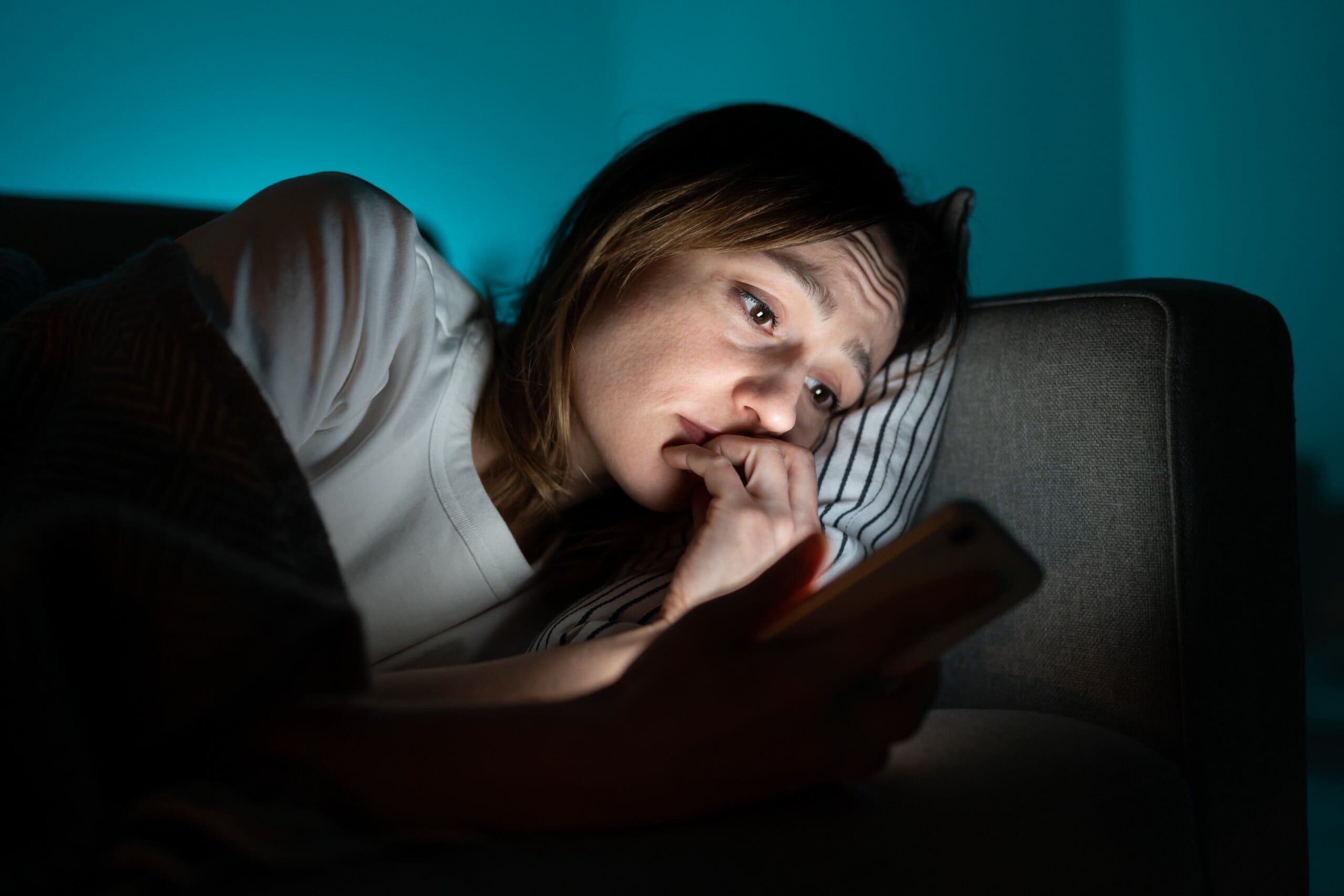 Woman layed down looking anxious at her phone screen.